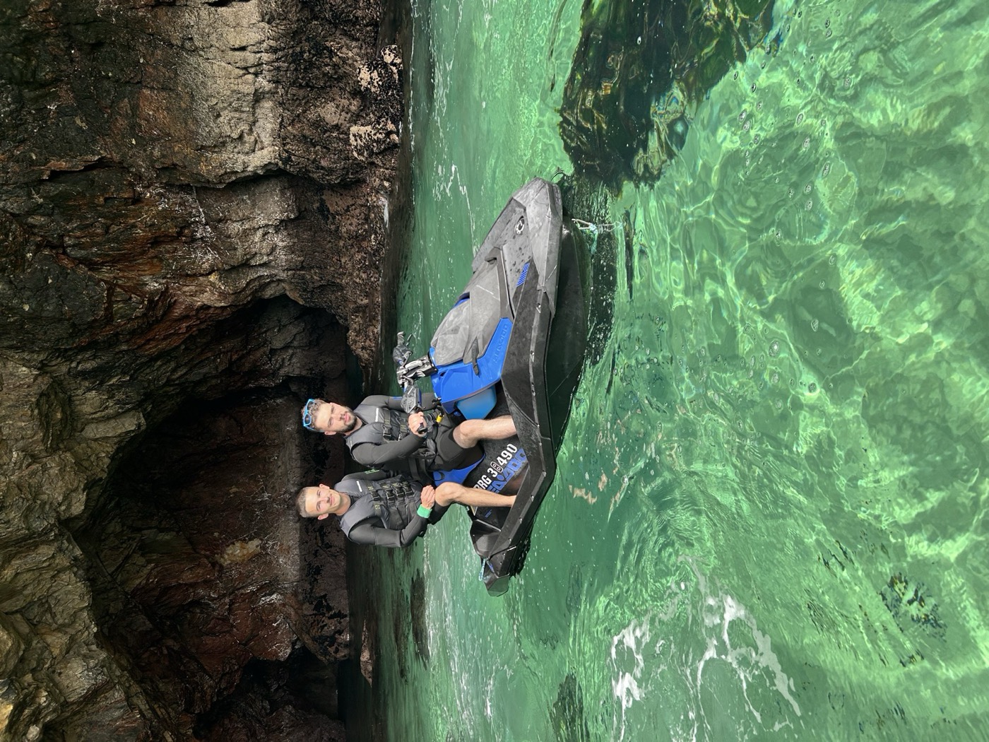 Dos personas en moto de agua junto a una cueva de agua turquesa